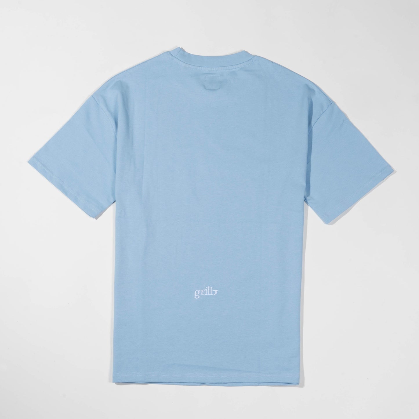 Parte trasera de la camiseta de manga corta azul celeste. Logo bordado en blanco y situado en la parte inferior de la camiseta. Corte oversized.