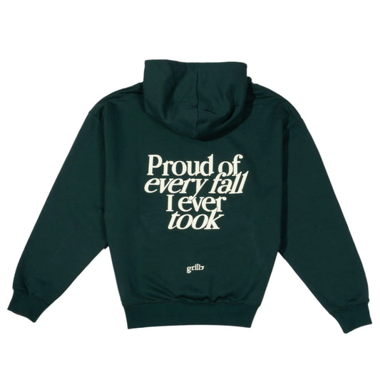 Parte trasera de la sudadera verde oscuro con capucha, 100% algodón. Frase 'proud of every fall i ever took' serigrafiada en color crema.