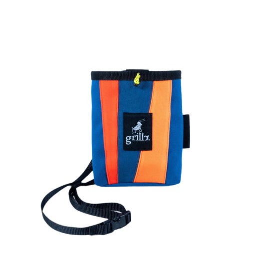 Magnesera en cordura 1000, en colores azul, naranja y rojo, con una cinta de nylon ajustable en la cintura, portacepillos elástico y un sistema de cierre mediante cordón que evita la pérdida de magnesio. Logo grillo bordado en el centro de la magnesera.