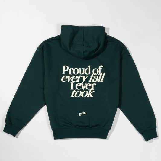 Parte trasera de la sudadera verde oscuro con capucha, 100% algodón. Frase 'proud of every fall i ever took' serigrafiada en color crema.